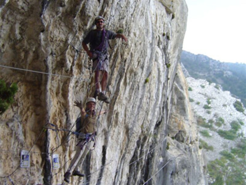 Escaladeur équipé pour la via ferrata progressant sur une paroi rocheuse avec un casque